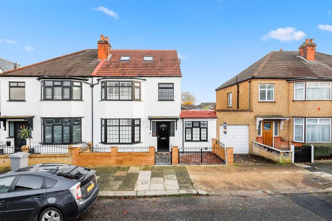 Two-story semi-detached house with a white exterior and black window frames, located on a residential street in Willesden Green. The property has a gated front yard with brick walls and is adjacent to a similar styled house with a brown exterior. A car is parked in front of the house on the street under a clear blue sky.