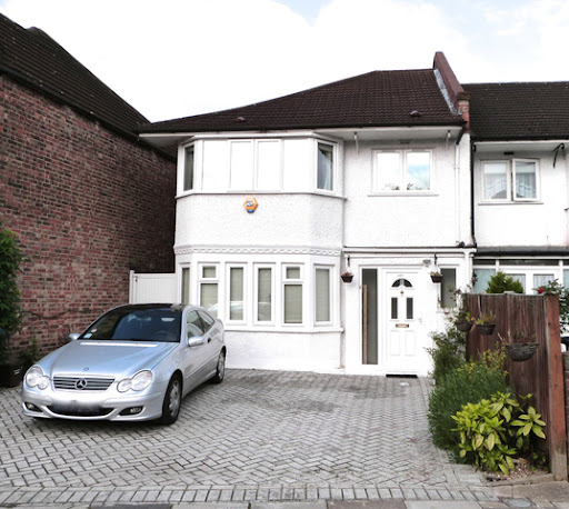 Two-story semi-detached house with a white exterior and bay windows, located on Hamilton Road in Golders Green. The property has a paved driveway with a silver car parked in front, and a small garden area to the side of the entrance.