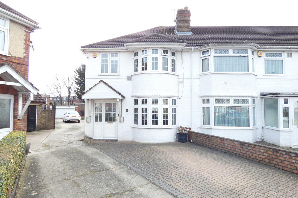 Two-story semi-detached house with a white exterior and bay windows, located on Sidmouth Avenue in Hounslow, London. The property has a paved driveway with a car visible at the back near a garage, and neighboring houses are partially visible on both sides.